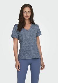 Koszulka sportowa z dekoltem w serek w melanzowym granatowym kolorze, krótki rękaw i lekko dopasowany krój, w zestawieniu z jasnoniebieskimi legginsami.