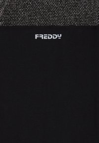 Camiseta negra con una textura suave que presenta un panel de malla plateada en la parte superior y el logo "FREDDY" en blanco.