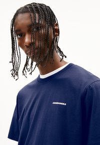 T-shirt en coton marine avec col rond blanc et logo brodé "ARMEDANGELS" sur la poitrine. Manches courtes et coupe décontractée.