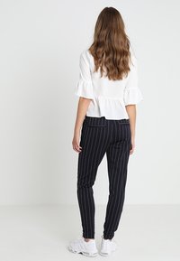 Biała bluzka peplum z falbaniastymi rękawami w połączeniu z czarnymi spodniami w prążki. Ma dopasowany krój i elastyczny pas. Białe sneakersy dopełniają stylizację.