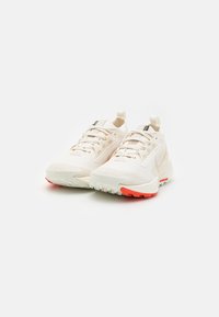 Baskets de sport beige clair avec tige en mesh, motif texturé et détails orange vif sur la semelle en caoutchouc. Équipées d'une languette pour un enfilage facile.