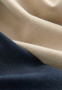 Baumwollstoff in Marineblau und Beige mit einer glatten Textur. Die Materialien sind übereinander geschichtet und zeigen subtile Muster sowie unterschiedliche Lichtreflexionen.