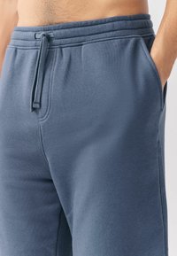 Pantalones de chándal azul oscuro hechos de tela suave, con una cintura elástica y un cordón, bolsillos laterales y una textura lisa.
