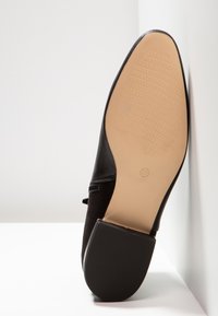 Semelle de chaussure habillée en cuir noir tournée vers le haut, montrant un dessous beige texturé et un talon noir avec un tampon de taille 37.