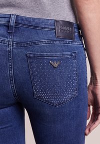 Jeans i mörkblått denim med en åtsittande passform. Har en bakficka prydd med små silvernitar och en läderlogotyp på midjebandet.