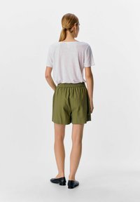 Haut rose clair à manches courtes et shorts vert olive avec une taille élastique. Les shorts ont des poches latérales et une coupe décontractée. Ballerines noires présentées.