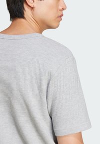 Svetlo šedá krátka tričko s krátkym rukávom vyrobené z textúrovanej tkaniny, so štýlovým okrúhlym výstrihom a jednoduchým dizajnom, ktorý zdôrazňuje pohodlie a priedušnosť.