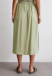 Light green, mid-length skirt with an elastic waistband and side slits, made of a smooth, flowy fabric. Worn with black sandals.