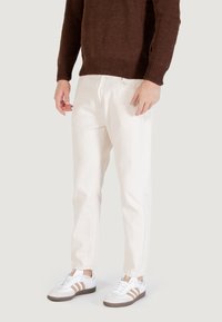 Pantaloni bianchi in cotone con una vestibilità dritta, abbinati a un maglione lavorato a maglia marrone e scarpe da ginnastica bianche. I pantaloni presentano tasche laterali e un taglio classico.