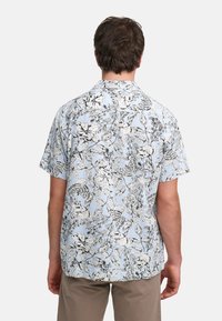 Kortermet skjorte med et blått og hvitt blomsterdesign med svarte kanter. Laget av lett stoff og har en uformell passform.