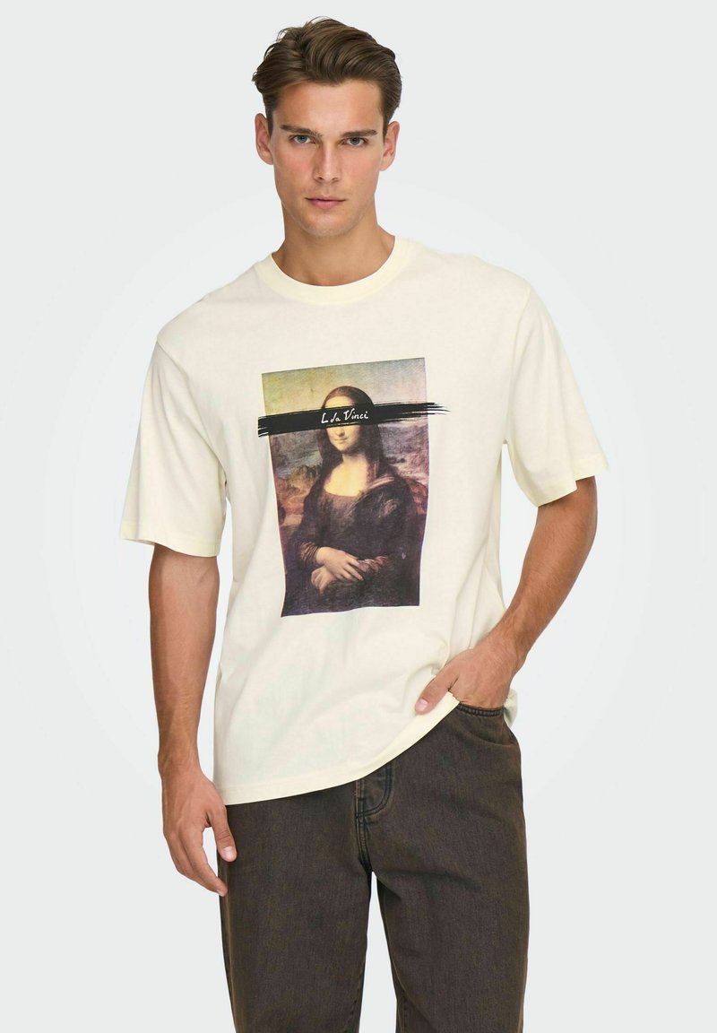 Kremfarvet t-shirt med korte ærmer, der har et trykt billede af Mona Lisa, suppleret med en sort penselstrøg og tekst ovenover.