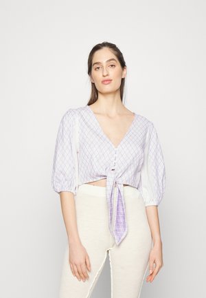 Blusa cropped em padrão xadrez roxo e branco, com mangas bufantes, decote em V e laço frontal; feita de tecido leve com uma textura suave.