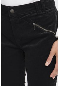 Fekete kordbársony nadrág, amelyen átlós cipzáras zseb és texturált anyag található. A derékrészen övbújtatók és gombos rögzítés kapott helyet.