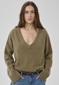Pull col en V vert olive en tissu doux avec ourlet côtelé et manches larges, associé à un jean en denim bleu taille haute et une ceinture noire.