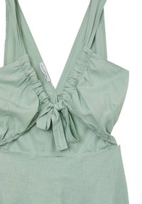 Vêtement sans manches vert clair avec tissu froncé au niveau de la poitrine, nœud noué devant et larges bretelles.