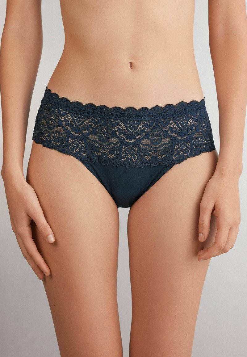 Las braguitas de encaje azul marino cuentan con una amplia cinturilla de encaje con patrones florales y bordes festoneados, complementadas por un cuerpo de tejido suave.