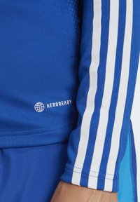 Blue athletic shirt featuring white stripes down the sleeves, made of textured fabric with an "AEROREADY" logo near the hem.