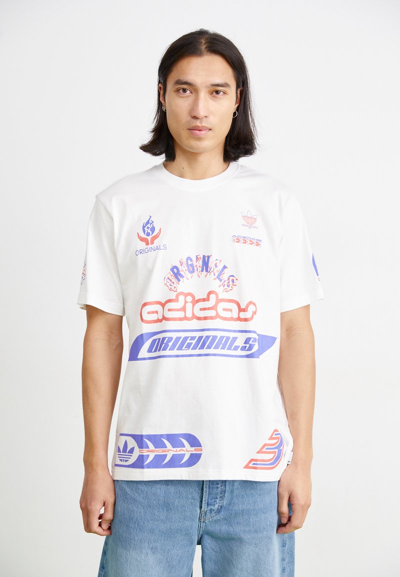 Balta medvilnė marškinėliai su ryškiu daugiaspalviu "adidas" prekės ženklu ir logotipais, su grafikos akcentais raudonos, mėlynos ir purpurinės spalvos. Trumpomis rankovėmis, laisvas kirpimas.