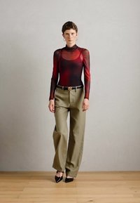 Top a maniche lunghe rosso e nero in mesh, design con collo alto, abbinato a pantaloni larghi a vita alta verde oliva e scarpe a punta nere.