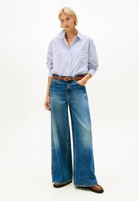 Lichtblauw en wit gestreept shirt met een kraag, gecombineerd met wijde blauwe jeans en een bruine riem. Glad denimtextuur, casual pasvorm.