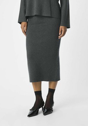 Woman wearing a knee-length dark gray pencil skirt, black sheer ankle socks, and black patent leather pointed-toe heels.