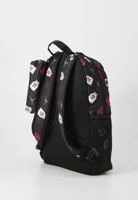Schwarzer Rucksack mit einem Netzrückenpaneel, roten und weißen Trikotmustern, verstellbaren Trägern und einem mit Reißverschluss belegten Hauptfach.