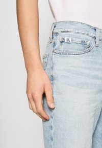 Jeans in denim blu chiaro con vestibilità dritta, dotati di etichetta con logo CK, accessori in argento e leggere sfumature nella trama del tessuto.