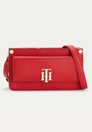 Sac bandoulière en cuir rouge avec une poche avant, logo "TH" doré et bandoulière réglable sur fond uni.
