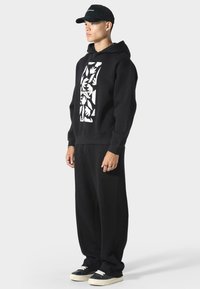 Sudadera negra con gráfico floral blanco, combinada con pantalones negros holgados. Acentuada con una gorra negra y zapatos negros con suelas blancas.