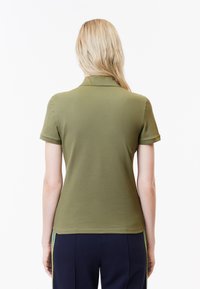 Olivgrön polotröja med krage, korta ärmar och en figursydd design. Slät textur med rena sömmar och inga synliga mönster.