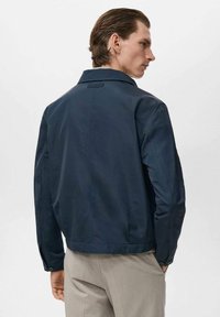 Chaqueta azul marino de tejido suave, con cuello, mangas largas, cierre de botones y un diseño cortado.