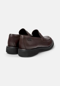 Ruske nahkaste loaferi z ravno črno podplatom, gledano od zadaj, prikazujejo eleganten dizajn in minimalno označevanje ob strani.