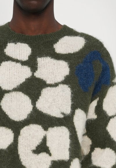 Suéter de punto verde con grandes manchas irregulares en blanco y azul, con una textura suave y peluda y un diseño de cuello redondo.