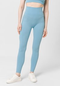 Světle modré legíny s vysokým pasem a ribbovanou texturou, kombinované s bílými teniskami. Design se vyznačuje hladkým, elastickým materiálem.