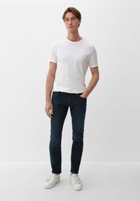 Witte katoen t-shirt, getailleerd ontwerp, gecombineerd met donkere blauwe jeans, slim fit. Witte sneakers maken de casual outfit compleet. Effen achtergrond.