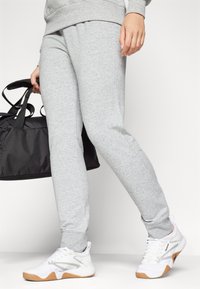Graue Sweatpants aus einem Baumwollmischgewebe. Mit elastischem Bund und schmal zulaufenden Beinen. Kombiniert mit weißen Sneakers und einer schwarzen Sporttasche.