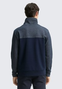 Polarowy pulower z wysokim kołnierzem, z ciemnoszarym górnym i granatowym dolnym fragmentem. Miękka tekstura i szczegóły z prążkowanymi mankietami.