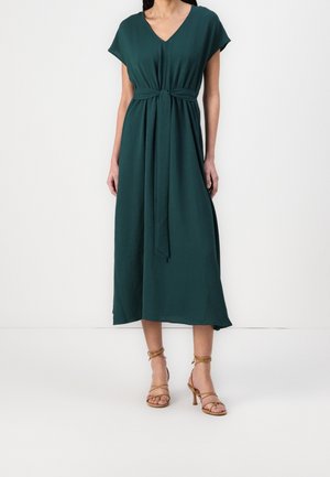 Mellemblå midi-kjole med V-udskæring, korte ærmer og detaljer med knyttet talje. Kombineret med beige sandaler med høje hæle og stropper.