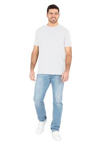 Lichtgrijs katoenen t-shirt met korte mouwen, gecombineerd met lichtblauwe jeans en witte sneakers. Staat tegen een witte achtergrond.