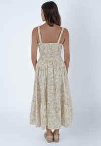 Beżowa maxi sukienka w wzory z marszczonym topem, cienkimi, marszczonymi ramiączkami i warstwową spódnicą. Noszona z sandałami na cienkich paskach w neutralnym kolorze.
