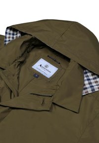 Olivgrüne Jacke mit Kapuze, ausgestattet mit einem karierten Futter und einem Etikett innen. Reißverschluss-Tasche vorne, glatte Textur und leichtes Material.