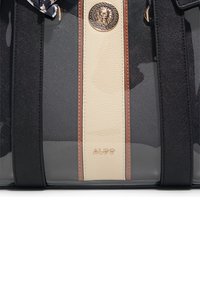 Borsa a mano in PVC nera e trasparente con un pannello centrale crema e dettagli marroni. Presenta un'emblema dorato di leone e tracolle a contrasto.
