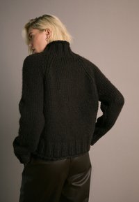 Maglione nero lavorato a maglia con collo alto, spalle scese e orlo a costine. Indossato con pantaloni in pelle scura, caratterizzati da una finitura testurizzata.