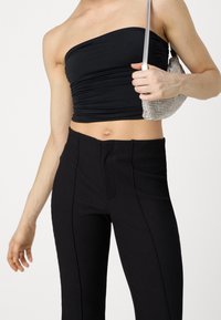 Zwarte strapless top van soepel stof met gerimpelde details. Hoge zwarte ribgebreide broek met naadaccenten, gecombineerd met een metallic handtas.