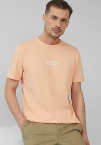 Lichtoranje katoenen t-shirt met ronde hals, korte mouwen en witte opdruk van het logo "s.Oliver Co. Established 1969" op de borst.