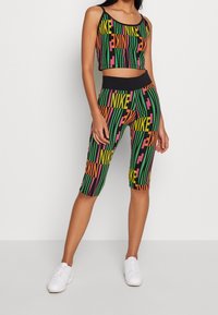 Top nero senza maniche e leggings al ginocchio presentano un audace motivo a strisce multicolori con il testo "NIKE" in arancione, rosa e verde.