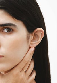 Pendiente de oro en la oreja derecha de un modelo, con forma de estrella. Piel suave y clara y cabello largo y oscuro. El modelo se toca el rostro con suavidad.