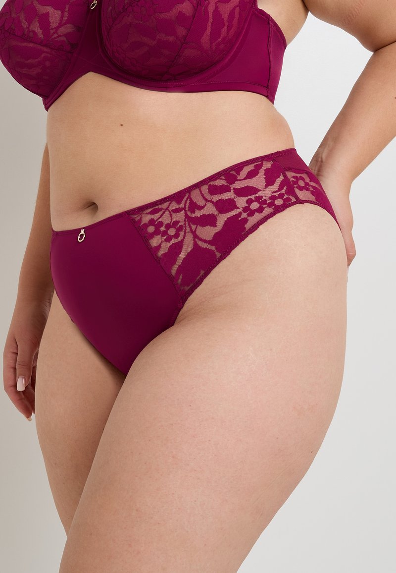 Gros plan sur une femme portant un ensemble coordonné en magenta profond, avec un soutien-gorge et une culotte ornés de détails en dentelle florale et d'un accent en charme doré sur la culotte.