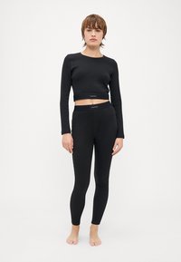 Crna dugak rukav cropped majica i usklađene tajice od rastezljivog materijala. Ima uski kroj s logotip trakom na struku.