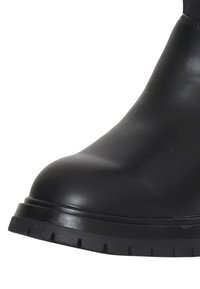 Stivale alla caviglia in pelle nera con punta tondeggiante, suola in gomma nera spessa con scanalature profonde e finitura liscia.